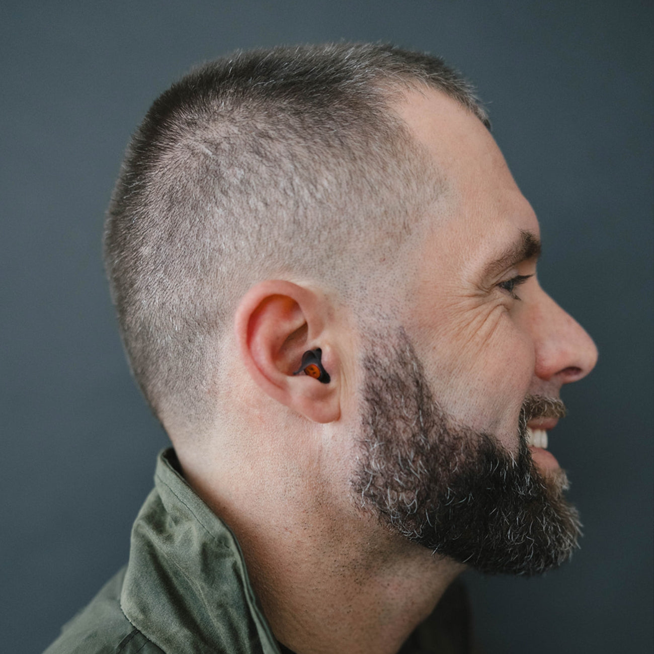 Man with a beard wearing Earpeace 24dB motorcycle earplugs and a jacket against a gray background
